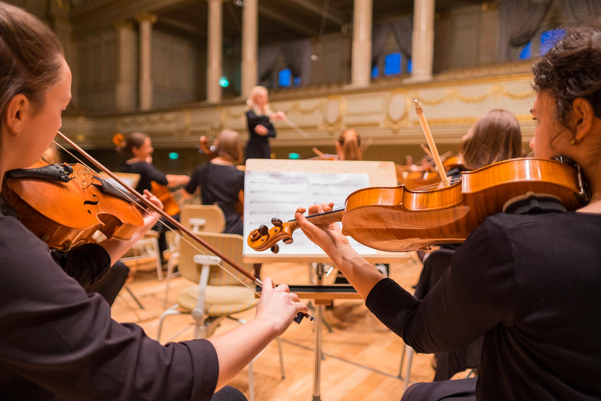 Jeunes musiciens jouant du violon sous la direction d'une cheffe d'orchestre