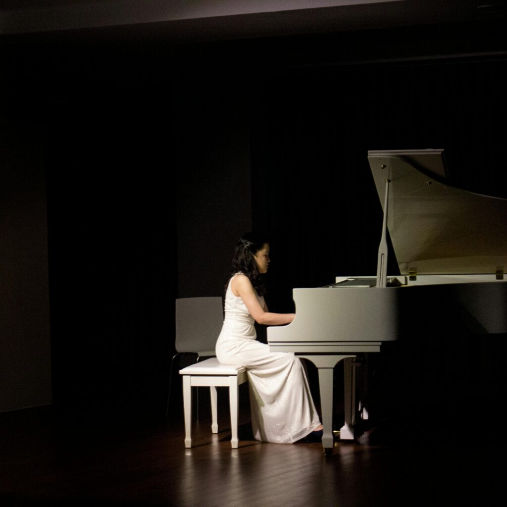Pianiste en robe blanche jouant sur un piano à queue blanc dans une salle obscure
